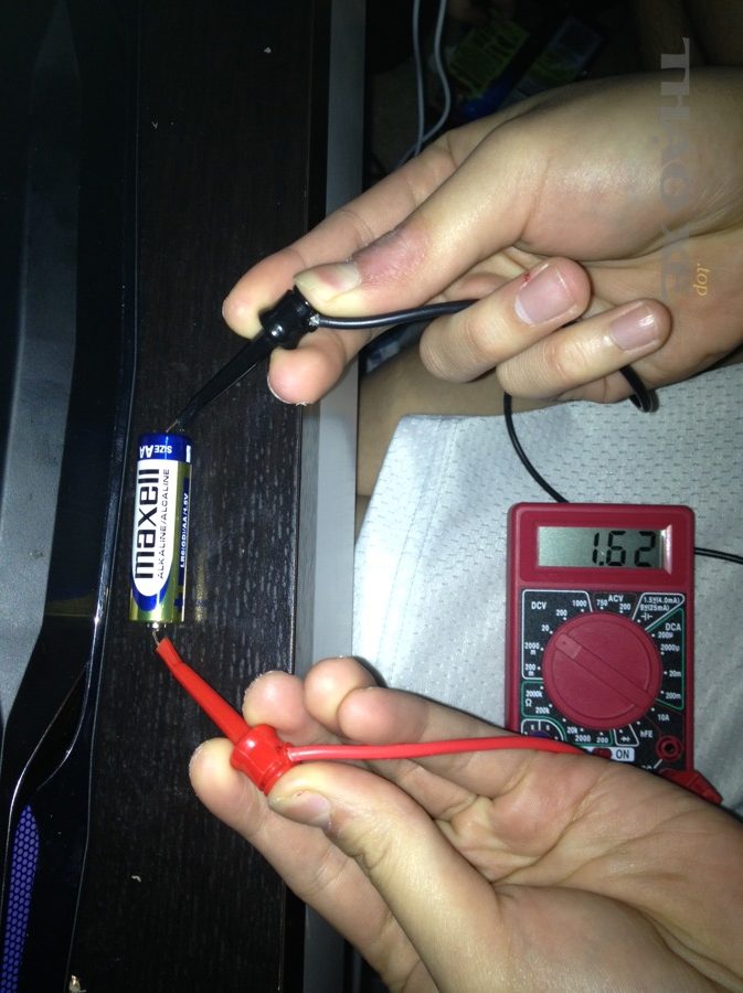 Minh họa dùng đồng hồ đo để kiểm tra điện áp (nguyên lý tương tự khi đo ắc quy)